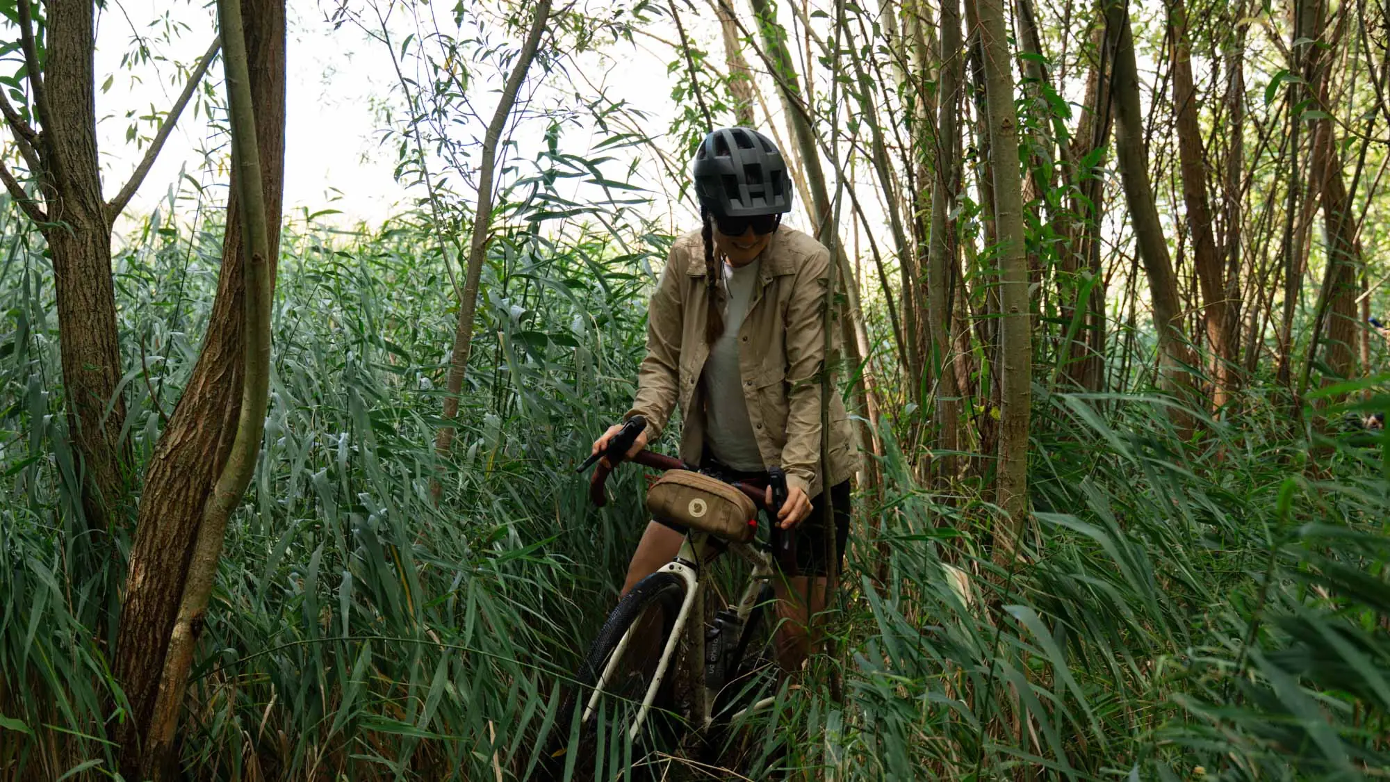 A woman stands on a Veloheld gravel bike, the iconX, amongst trees and reeds