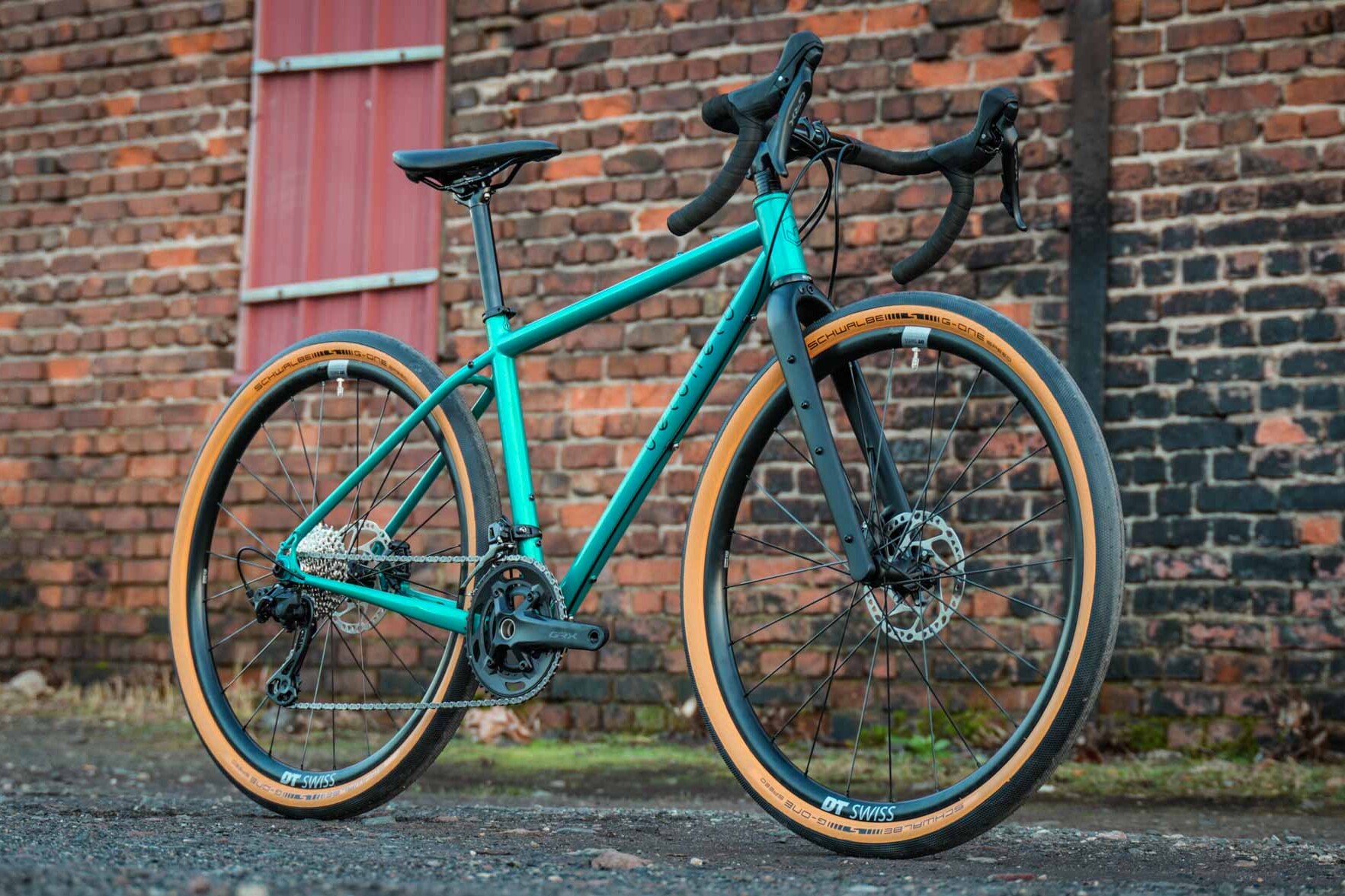 Gravel bike by veloheld in blue-green in front of a brick wall