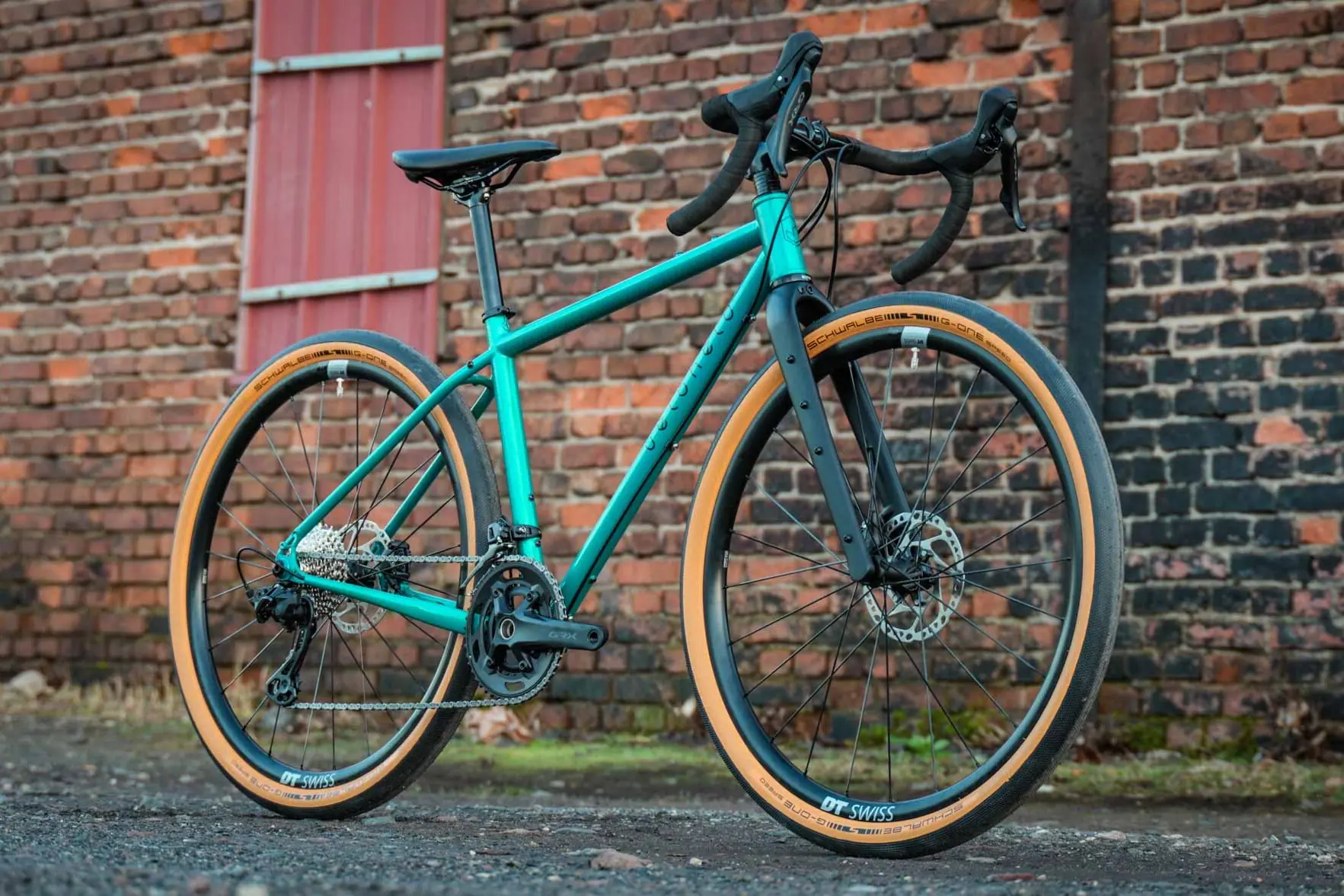 Gravel bike by veloheld in blue-green in front of a brick wall