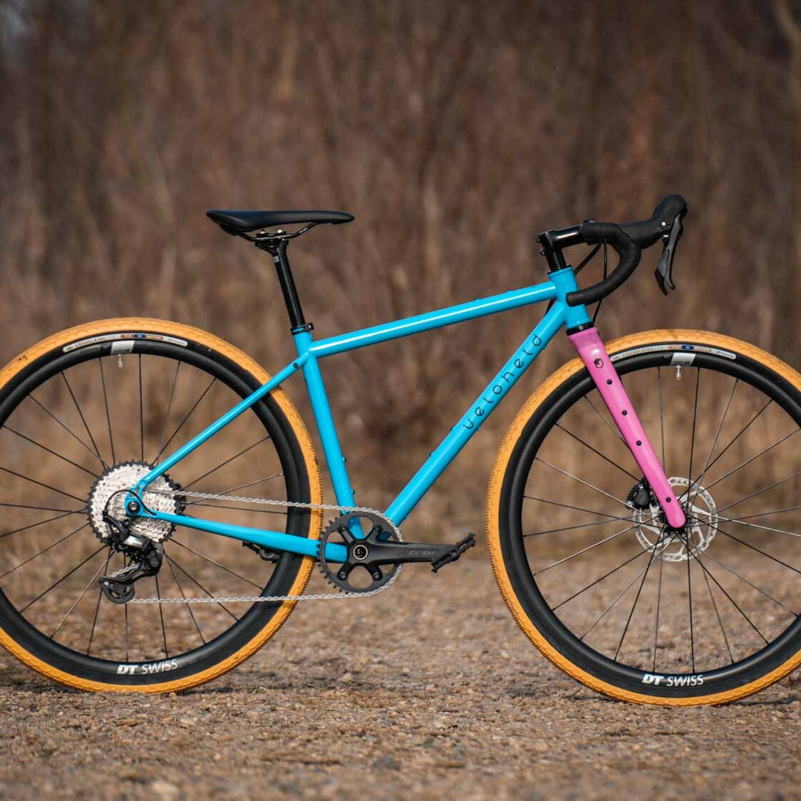 veloheld iconX Custom Gravel Bike Bubblegum Color Design Detail with blue frame, pink fork, and yellow tires - Complete bike standing on gravel