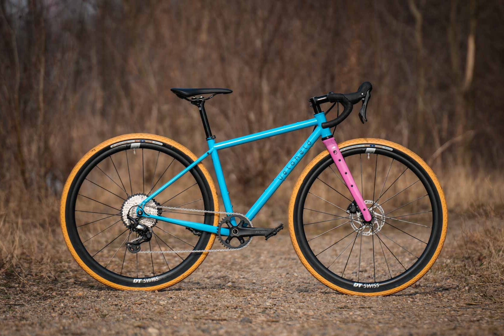 veloheld iconX Custom Gravel Bike Bubblegum Color Design Detail with blue frame, pink fork, and yellow tires - Complete bike standing on gravel