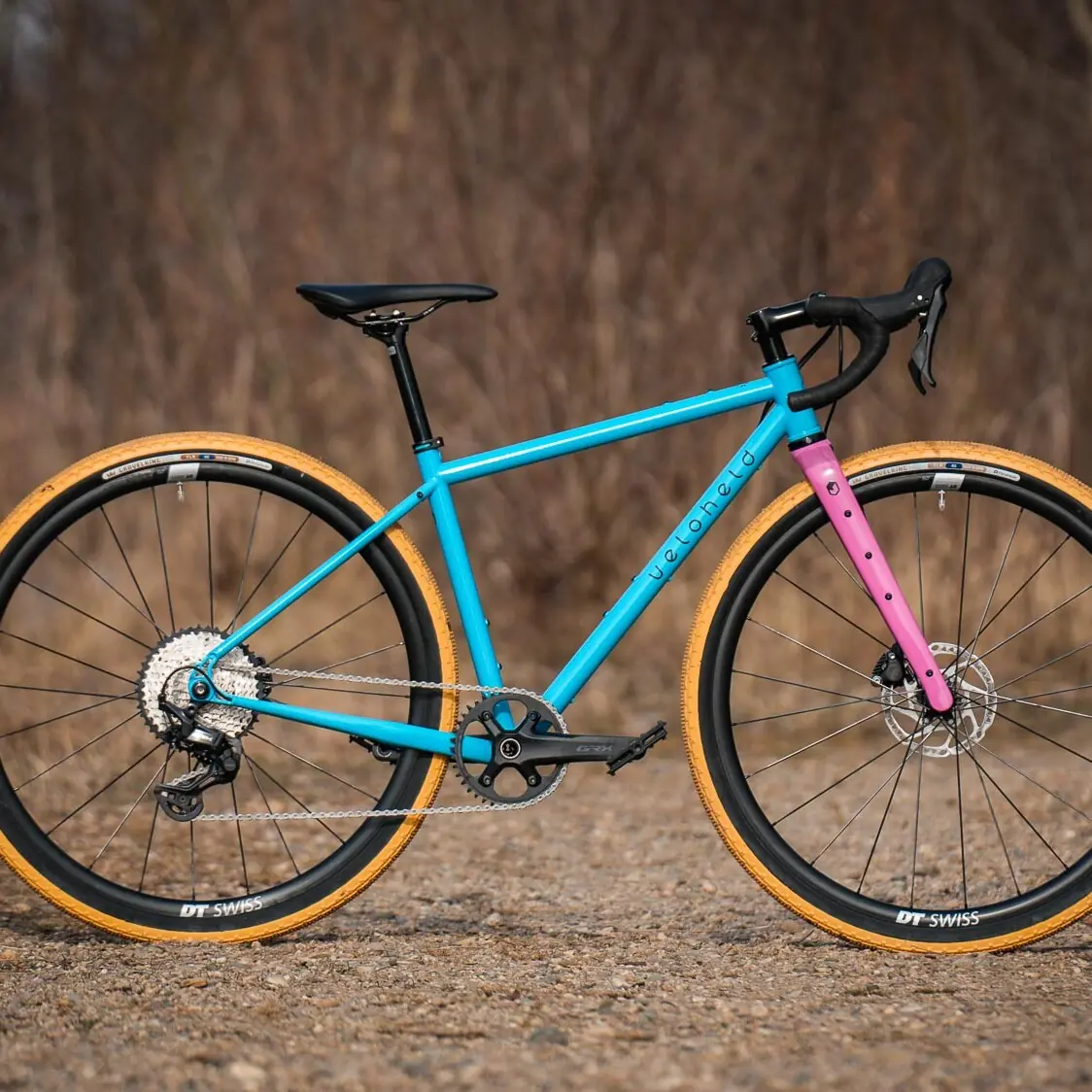 veloheld iconX Custom Gravel Bike Bubblegum Color Design Detail with blue frame, pink fork, and yellow tires - Complete bike standing on gravel
