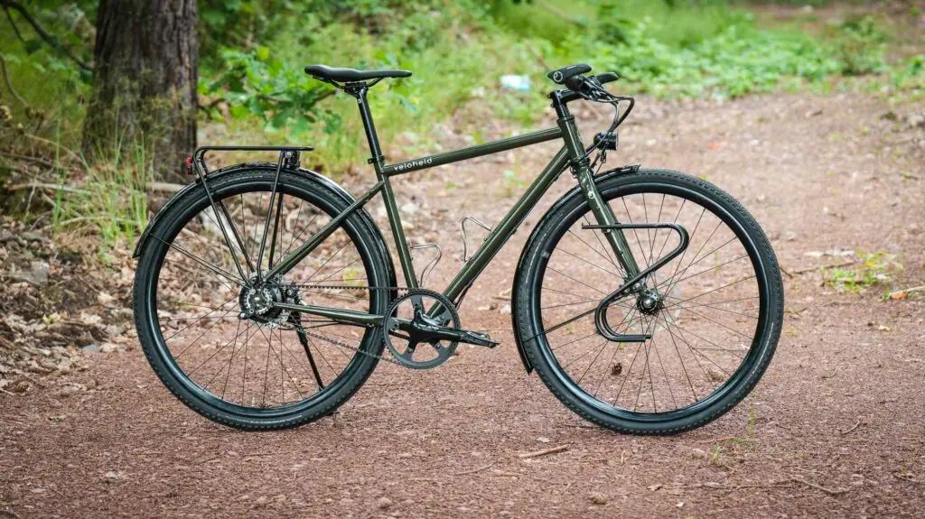 veloheld.alleyX Komplettrad mit Rohloff-Nabenschaltung, Schutzblechen und Gepäckträger als Komplettansicht auf einem Waldweg.